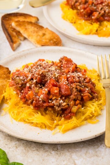 Two plates of spaghetti squash bolognese, toast, basil, and a glass of white wine.