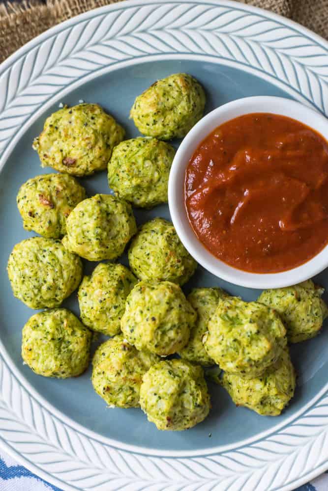 Top shot of Simple Cheesy Cauliflower Broccoli Tots served on a blue plate with a bowl of marinara sauce on the right.