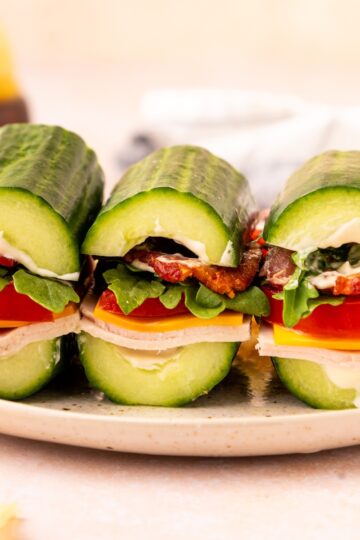Three cucumber subs filled with lettuce, tomato, bacon, and cheese on a white plate.