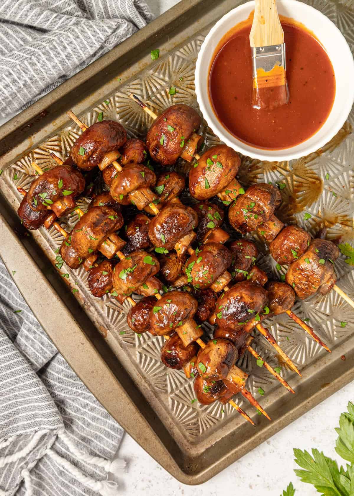 BBQ Mushrooms grilled on skewers with barbecue sauce and a brush on a baking tray.