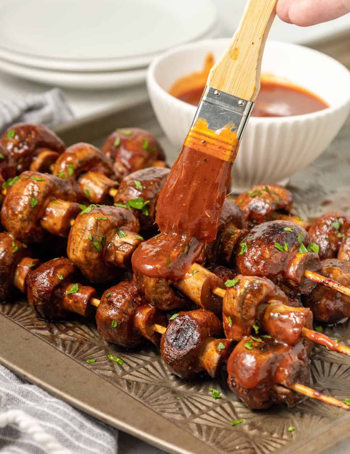 BBQ Mushrooms skewers being brushed with barbecue sauce on a tray.