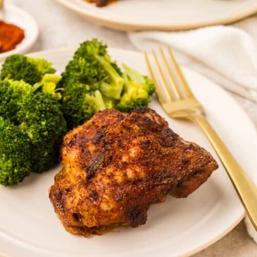 Paprika chicken thigh with steamed broccoli served on a plate with a gold fork.