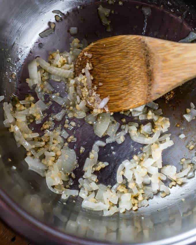 Top shot of a pot with sautéing onions and minced garlic with a wooden spoon.