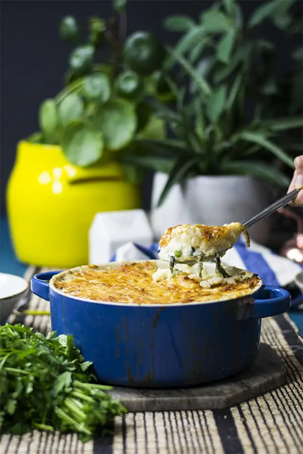 Keto fish pie in a blue baking dish surrounded by fresh herbs and potted plants with a blue background.