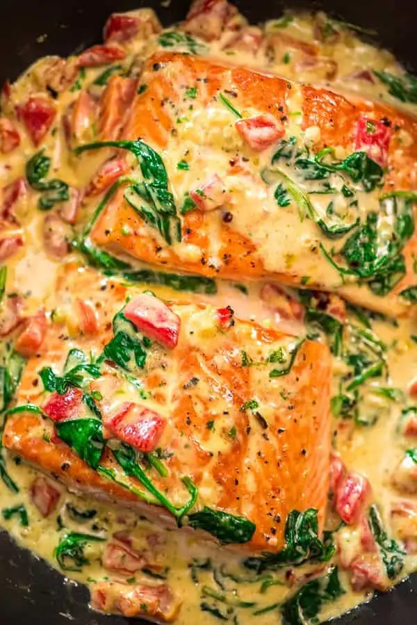 Salmon in a creamy roasted spinach and pepper sauce in a black skillet. 