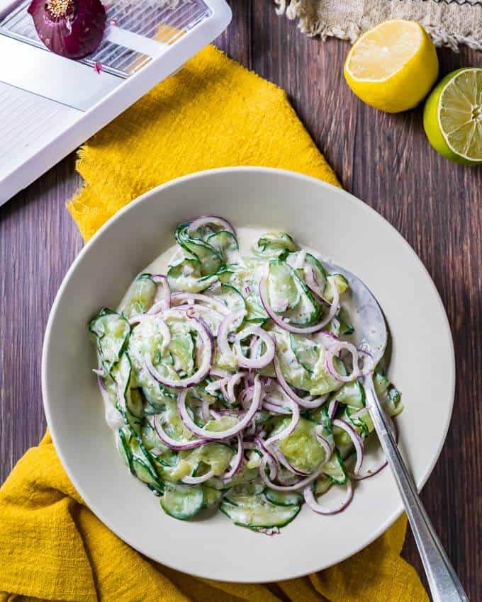 cucumber onion salad in a cream colored bowl on top of a yellow tea towel