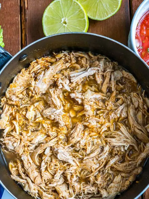 mexican shredded chicken in a pot, fresh lime visible on the side