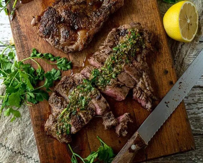 top shot of a sliced steak on a wooden board, topped with chimichurri sauce