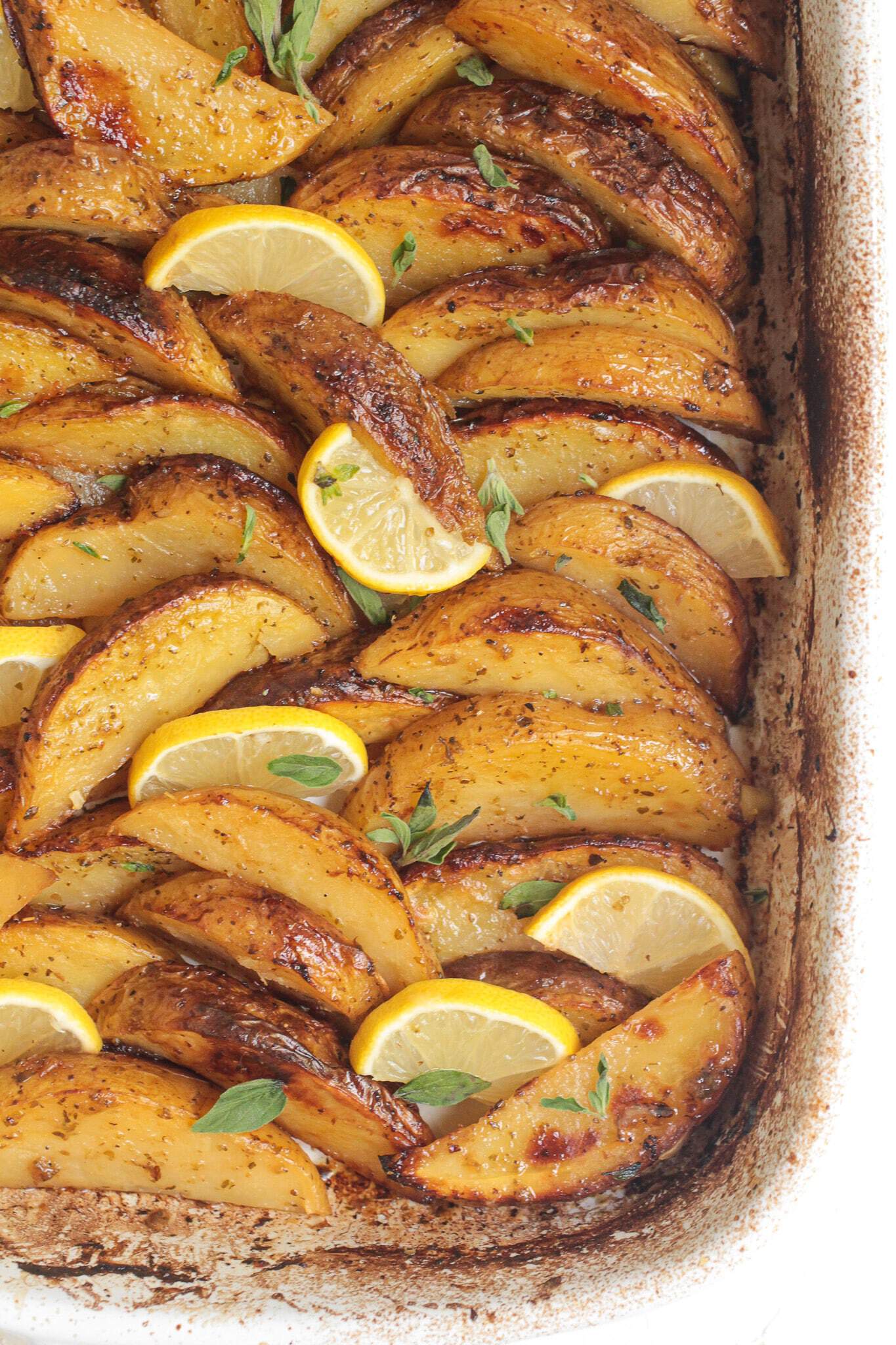 Easy side dish of roasted potato wedges with lemon slices and herbs in a white baking dish.