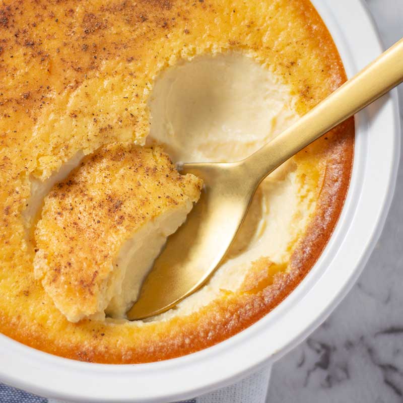 Egg custard keto Thanksgiving dessert being sccoped with a spoon in a white baking dish.