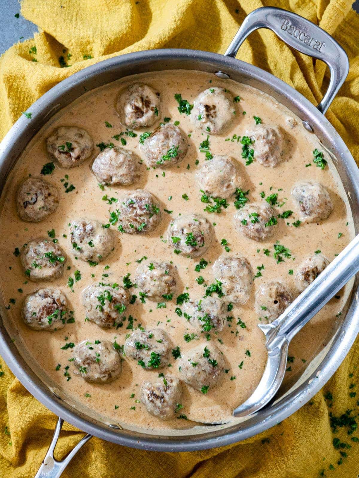 Keto swedish meatballs topped with fresh chopped herbs in a skillet on a yellow kitchen towel.