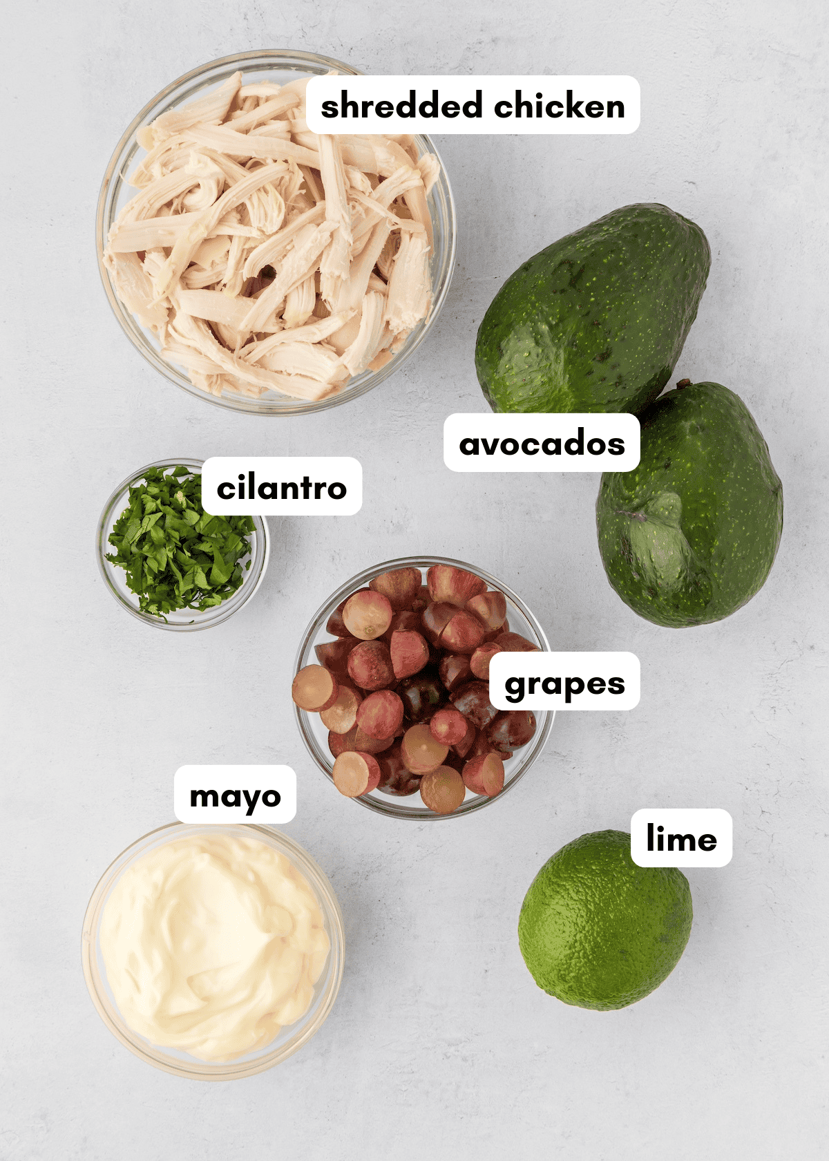 Bowls of Avocado Chicken Salad with cilantro, grapes, mayo, and fresh lime on a white surface.