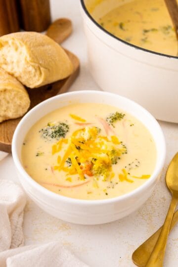 Bowl of Broccoli Cheddar Soup topped with shredded cheese, served with bread on the side.