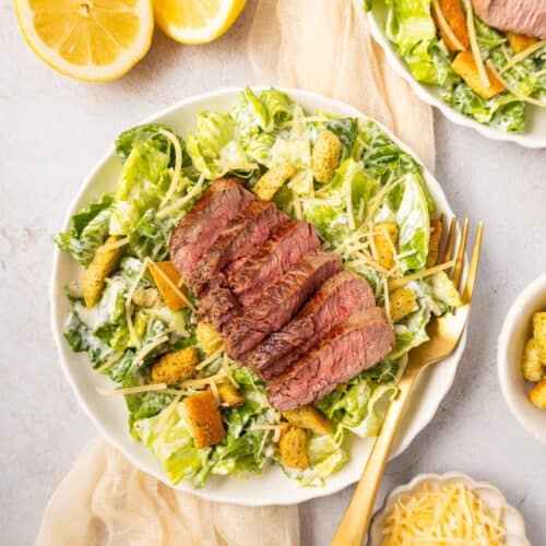 Steak Caesar Salad topped with croutons and parmesan, served with fresh lemon halves.