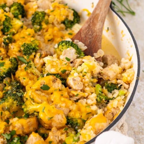 A casserole dish with chicken broccoli and rice, topped with melted cheese and stirred by hand.