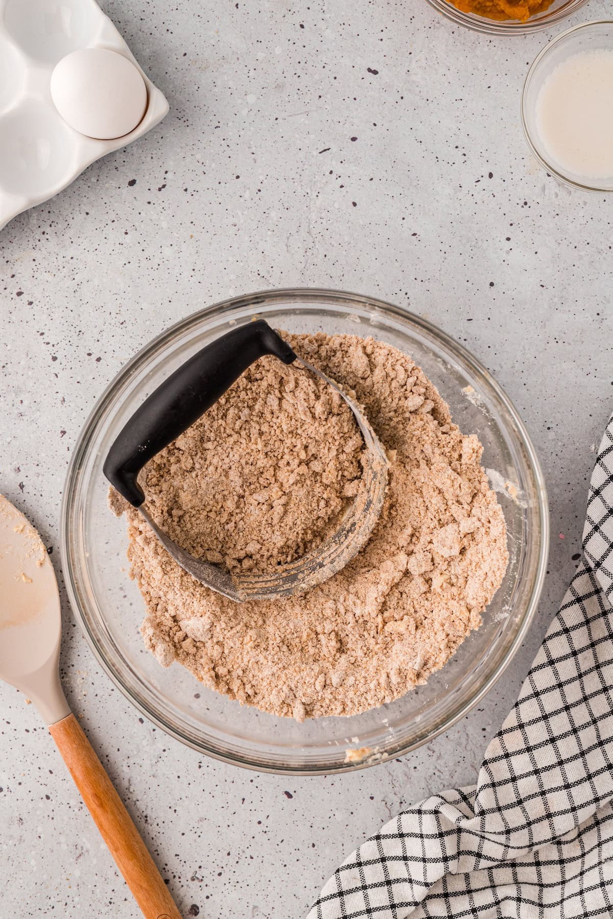 A glass bowl with crumbly dough for Gluten-Free Pumpkin Scones, plus an egg and a spatula.