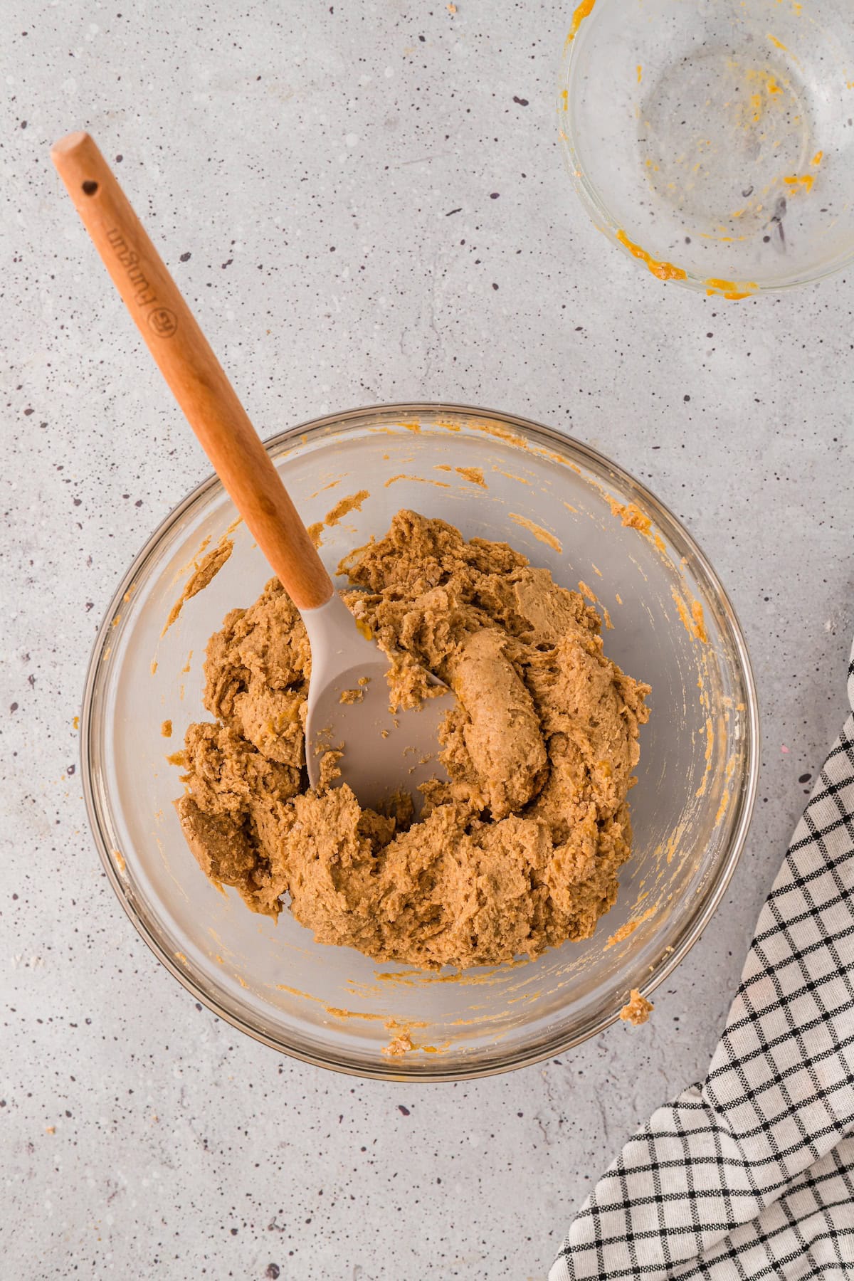 A glass bowl with Gluten-Free Pumpkin Scones dough and a spatula on a light countertop.