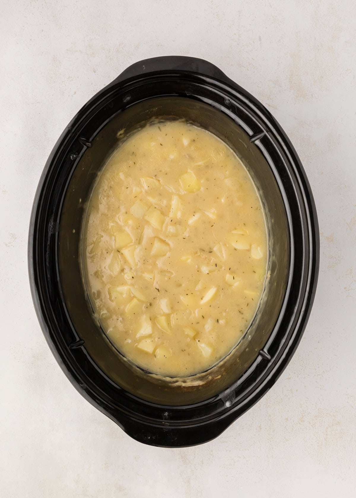 Soup added to crockpot with potatoes, thyme, salt, and pepper.