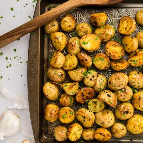 Garlic Roasted Potatoes on a baking sheet, garnished with herbs and served with a wooden spatula.