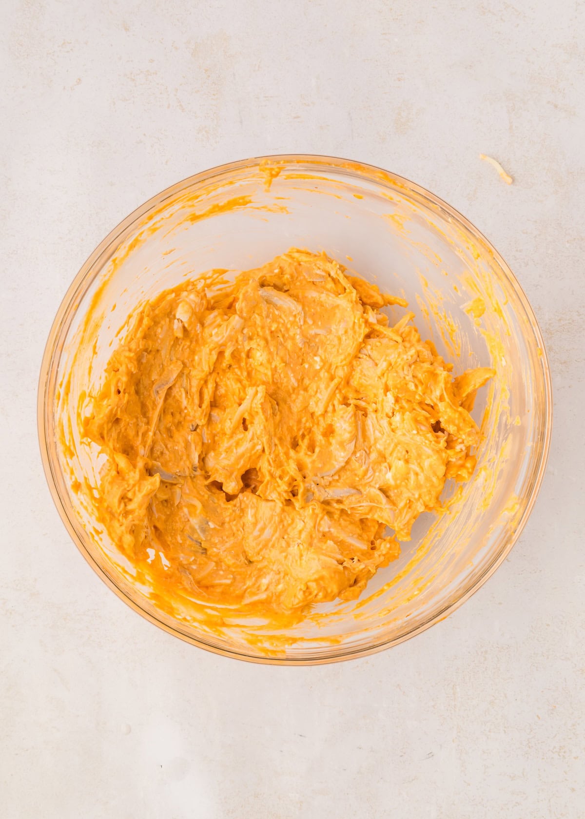 A glass bowl filled with creamy Buffalo Chicken Stuffed Peppers mixture on a light surface.