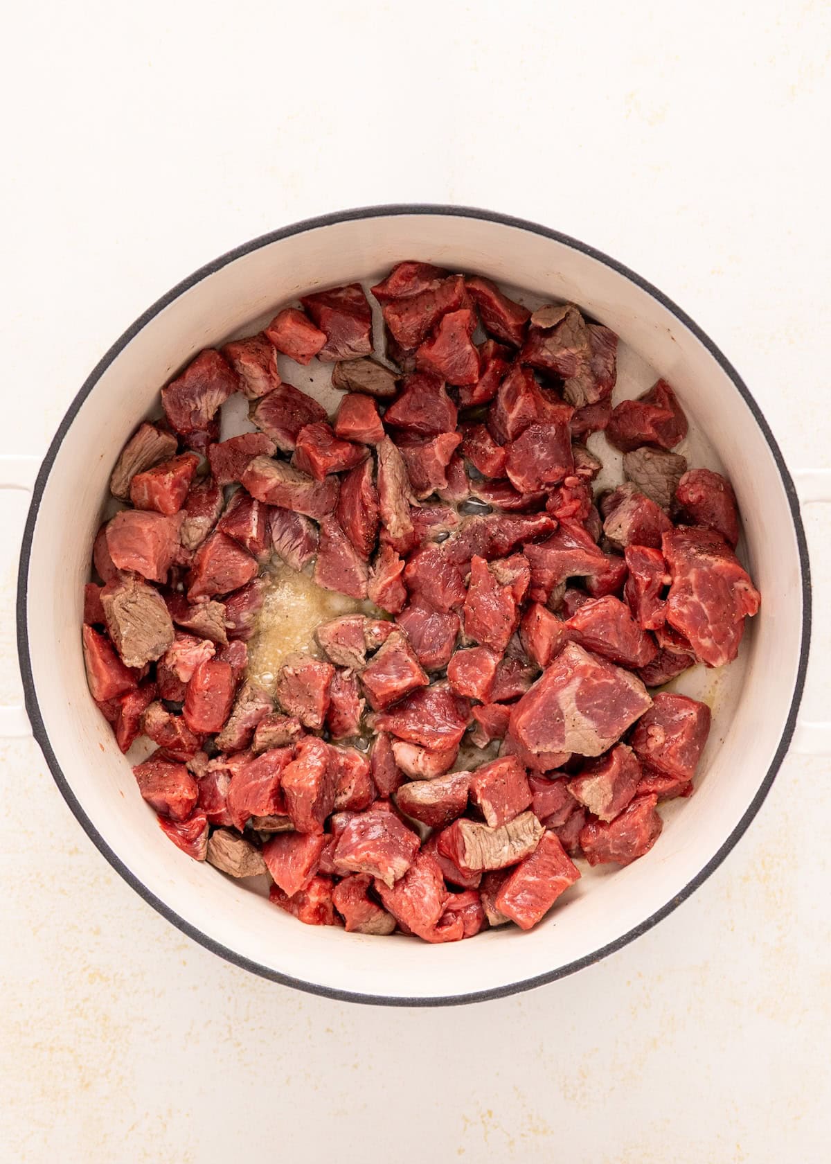 Chunks of raw beef in a white pot, ready to become a hearty Beef Vegetable Stew.