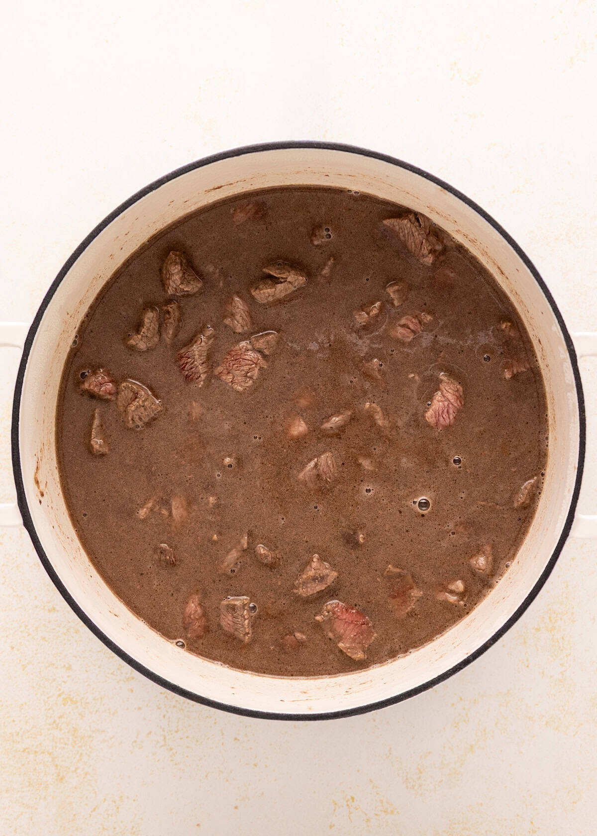 Beef Vegetable Stew simmering in a round white pot on a white surface.