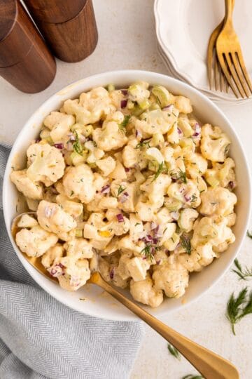 Cauliflower Salad with fresh herbs and dressing, served beside plates and elegant gold forks.