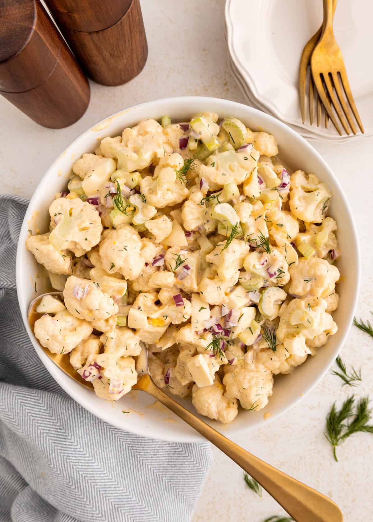 Cauliflower Salad with fresh herbs and dressing, served beside plates and elegant gold forks.