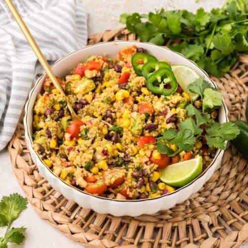 Southwest Quinoa Salad in a white bowl with serving spoon, garnished with lime and cilantro.
