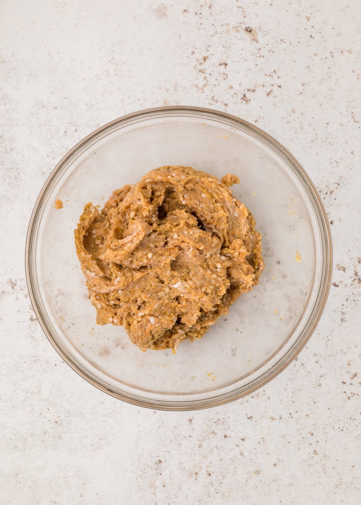 A glass bowl filled with BBQ Chicken Meatballs mixture on a light speckled surface.