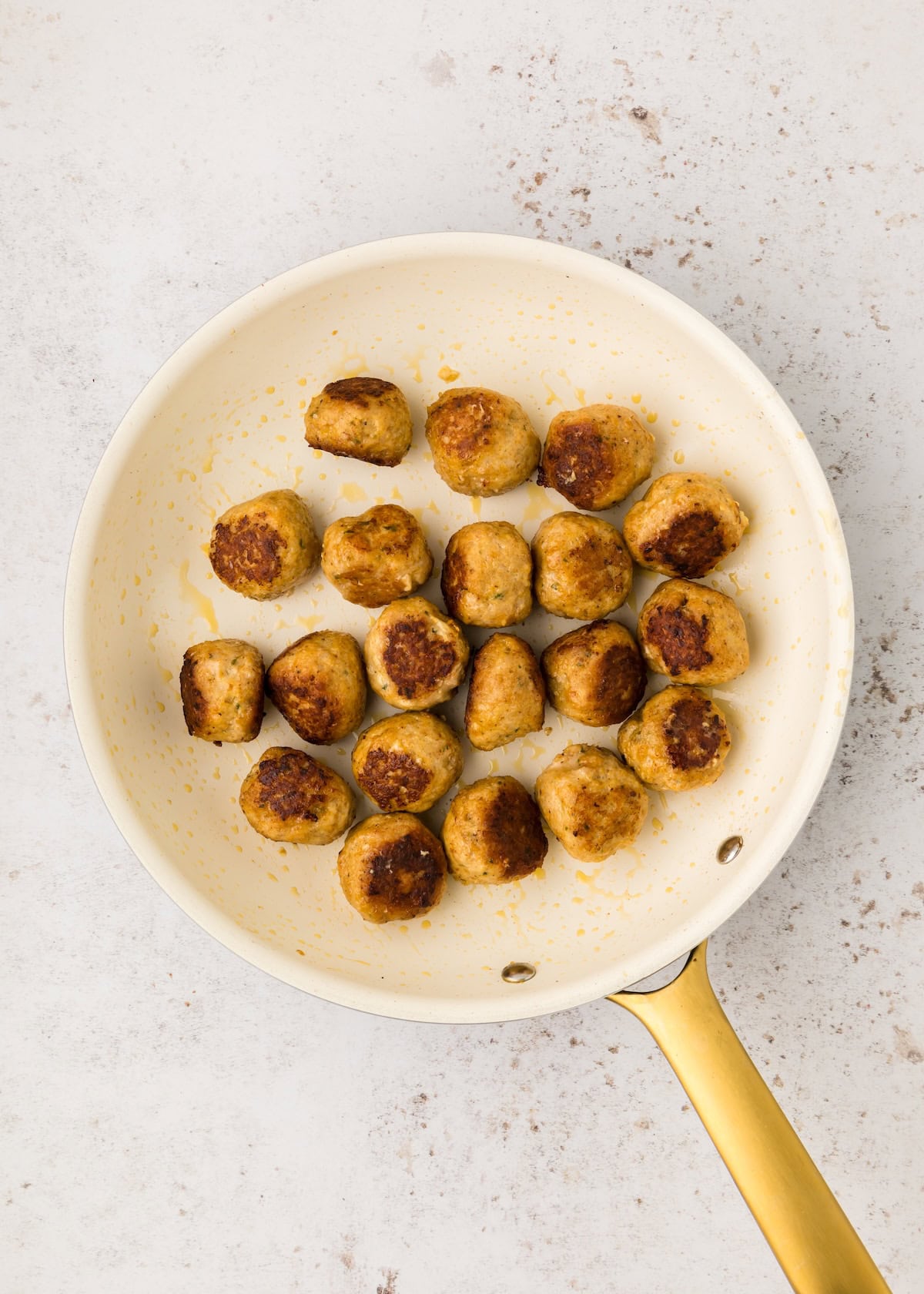 BBQ Chicken Meatballs sizzling in a white frying pan with a gold handle.