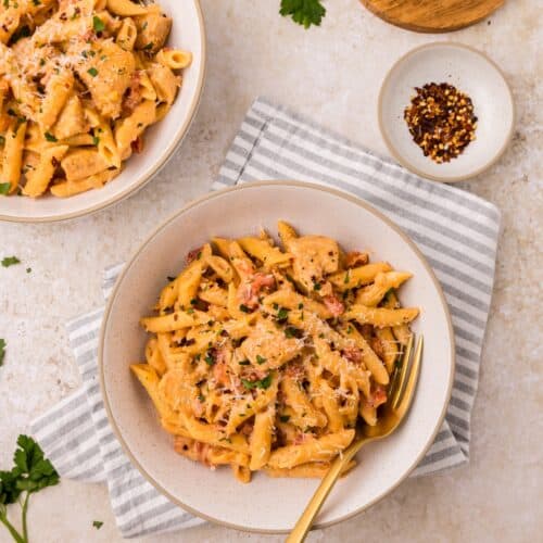 Two bowls of creamy Cajun Chicken Pasta with herbs, cheese, and a gold fork on a striped napkin.