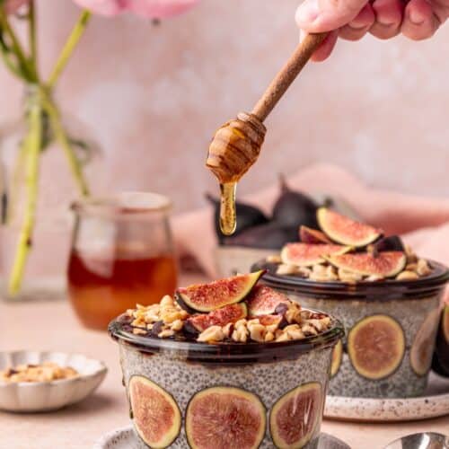 A hand drizzles honey over Fig Chia Pudding bowls topped with figs and nuts.
