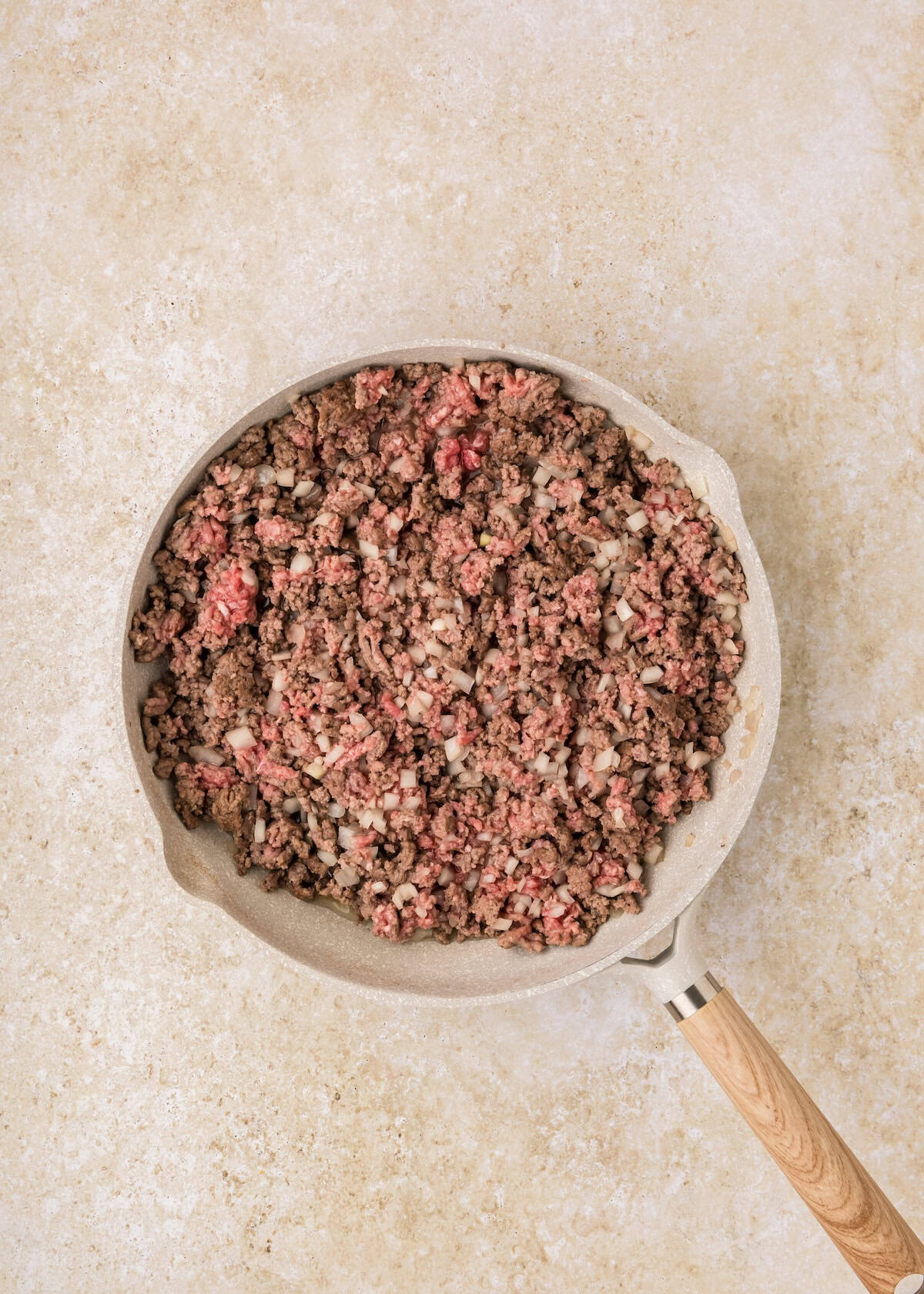 Ground beef and diced onions cooking for a tasty Sloppy Joe Casserole in a skillet.