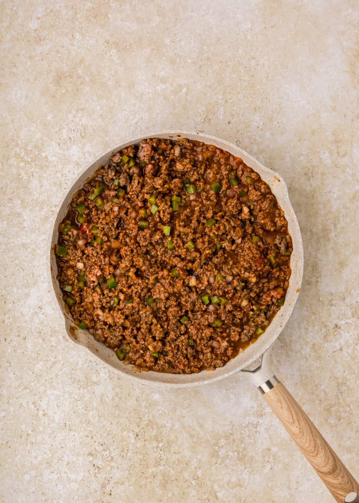 Cooked ground beef with diced green peppers for a tasty Sloppy Joe Casserole in a skillet.