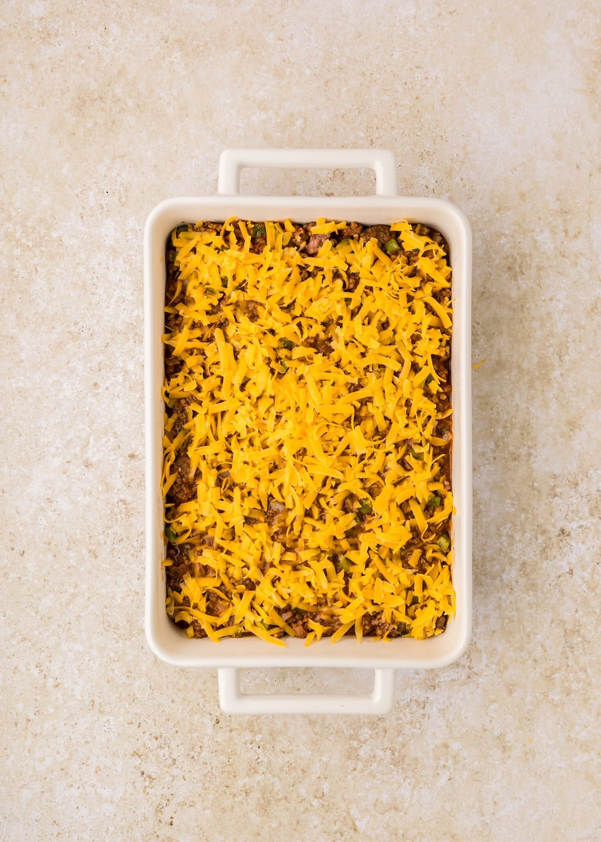 Rectangular Sloppy Joe Casserole topped with a layer of shredded cheddar cheese.