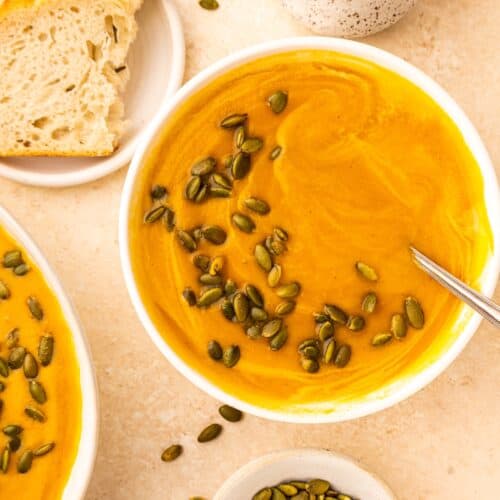 Bowl of Crockpot Sweet Potato Soup topped with pumpkin seeds, with bread and seeds on the side.