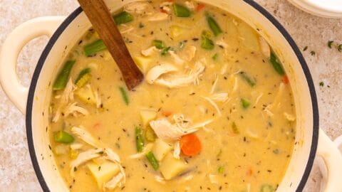 A pot of creamy leftover turkey stew with vegetables and a wooden spoon, on a light countertop.