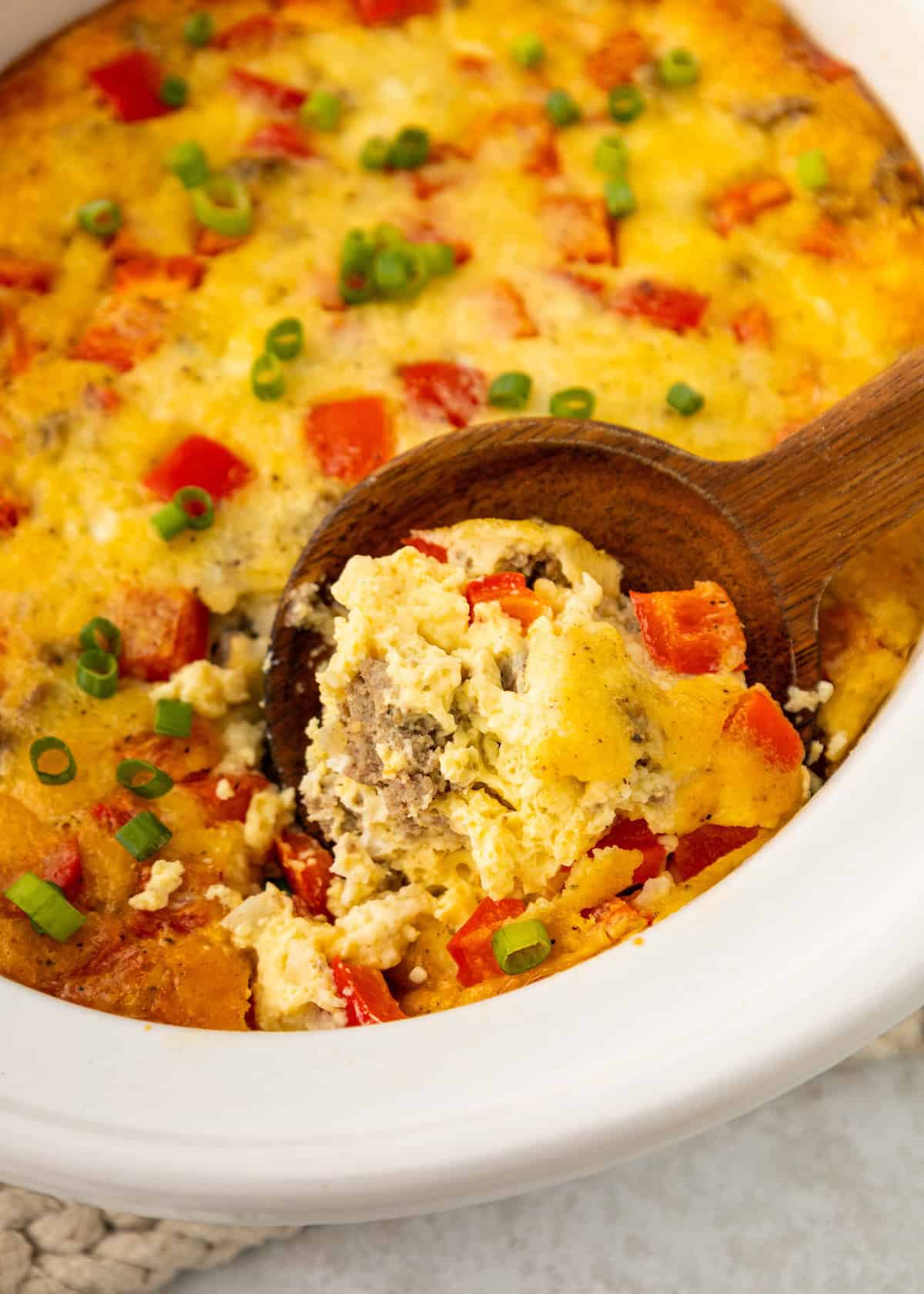 Scooping casserole out of the crockpot with a wooden serving spoon.