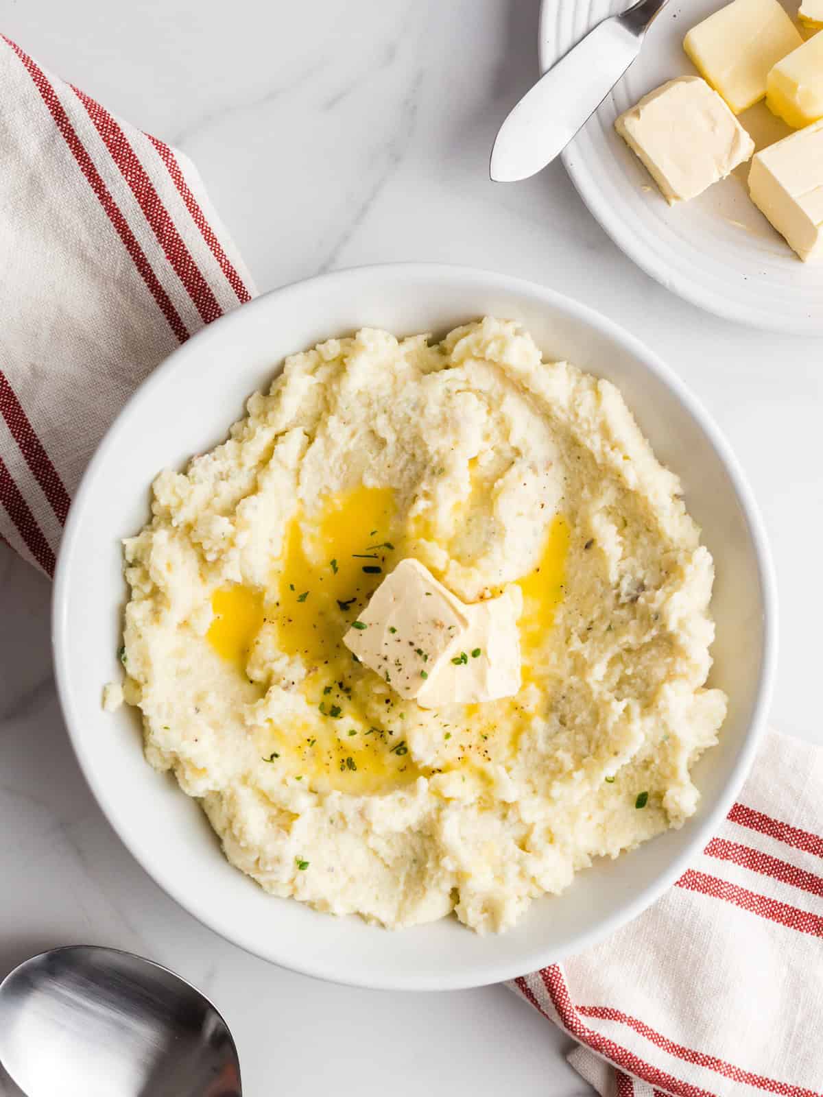 Bowl of mashed potatoes with melting butter and herbs on top, next to a red-striped napkin.