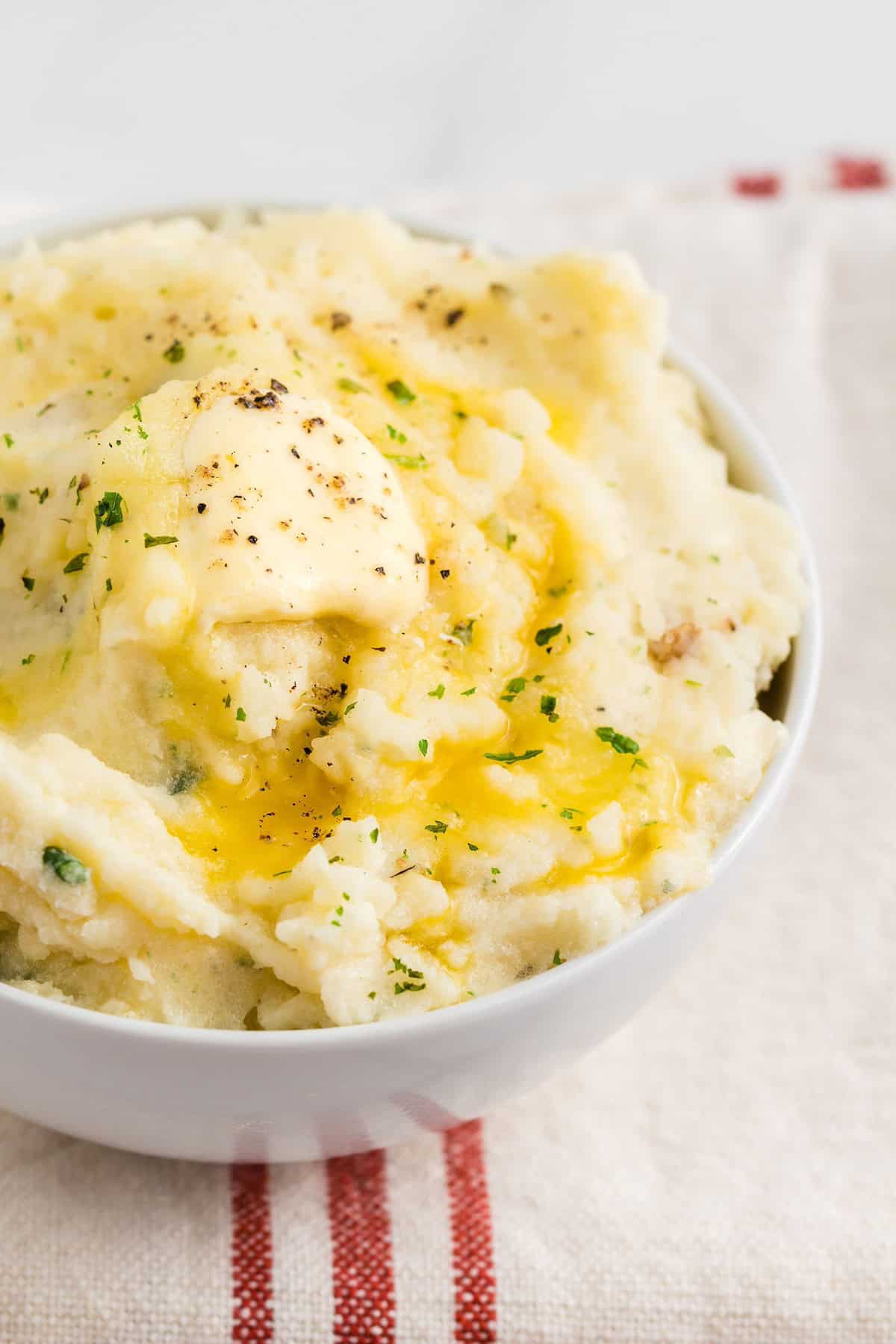 Bowl of mashed potatoes with melted butter, herbs, and black pepper on top.