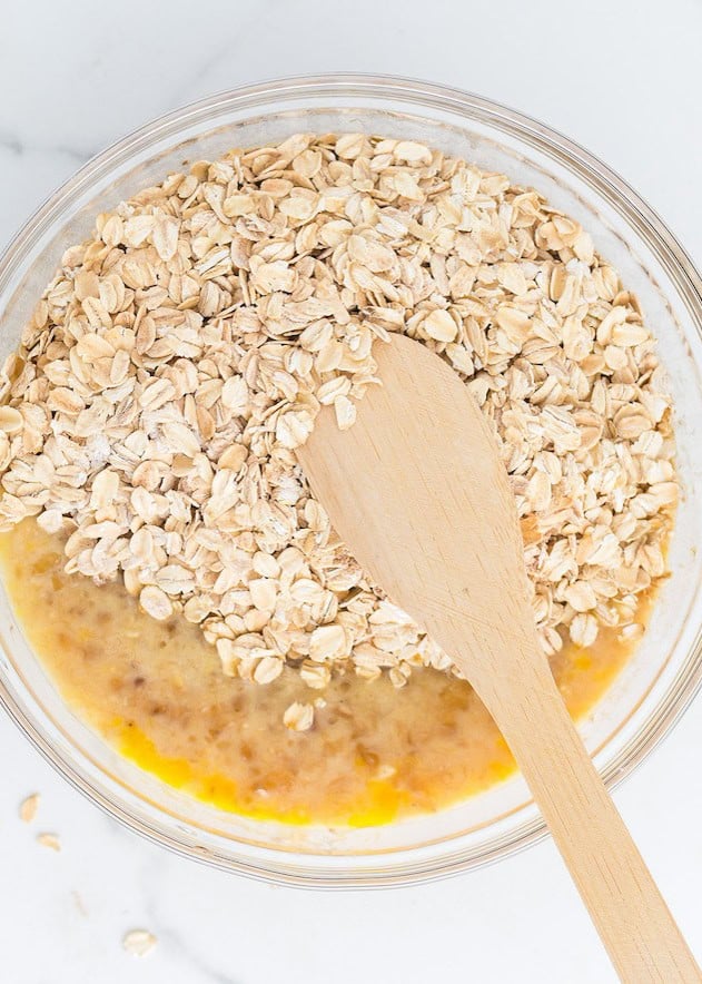 A bowl with oats, mashed banana, and a wooden spoon on a white surface.