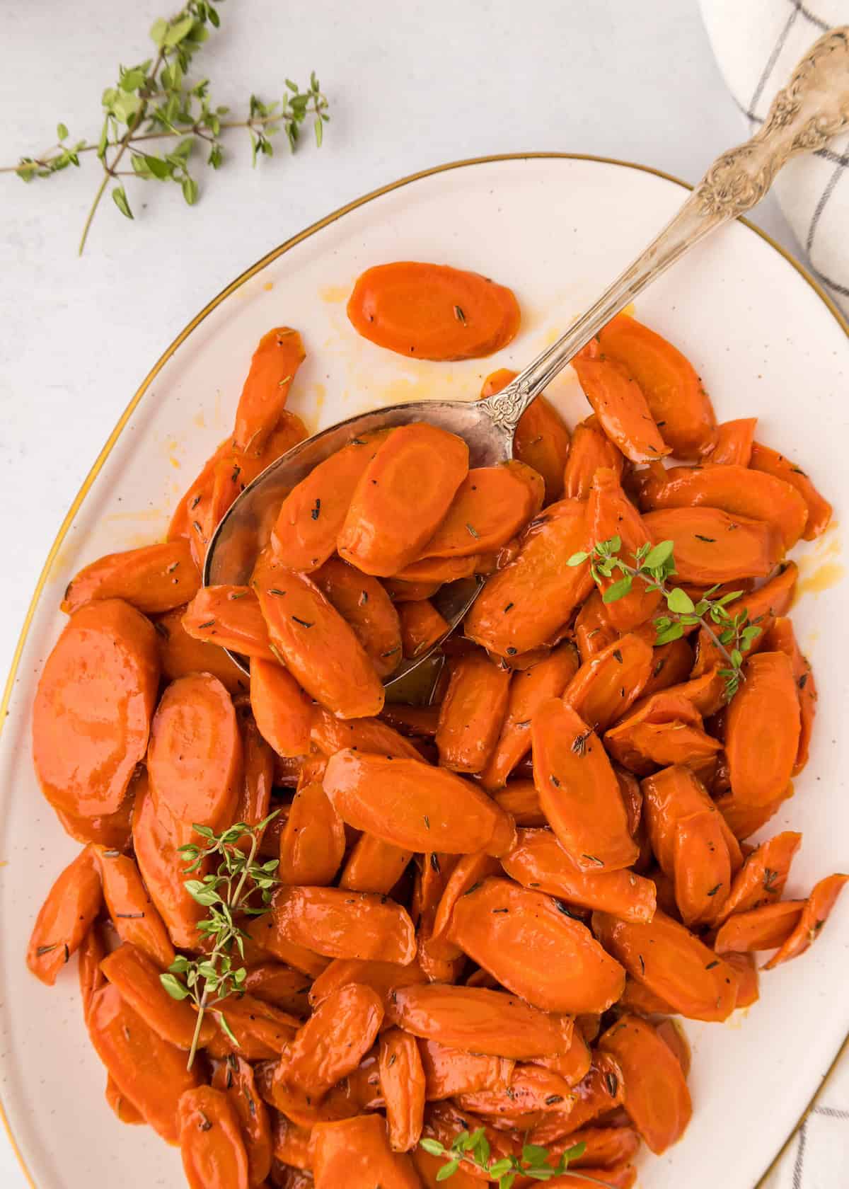 Sliced glazed carrots garnished with fresh herbs on a white plate, served with a spoon.