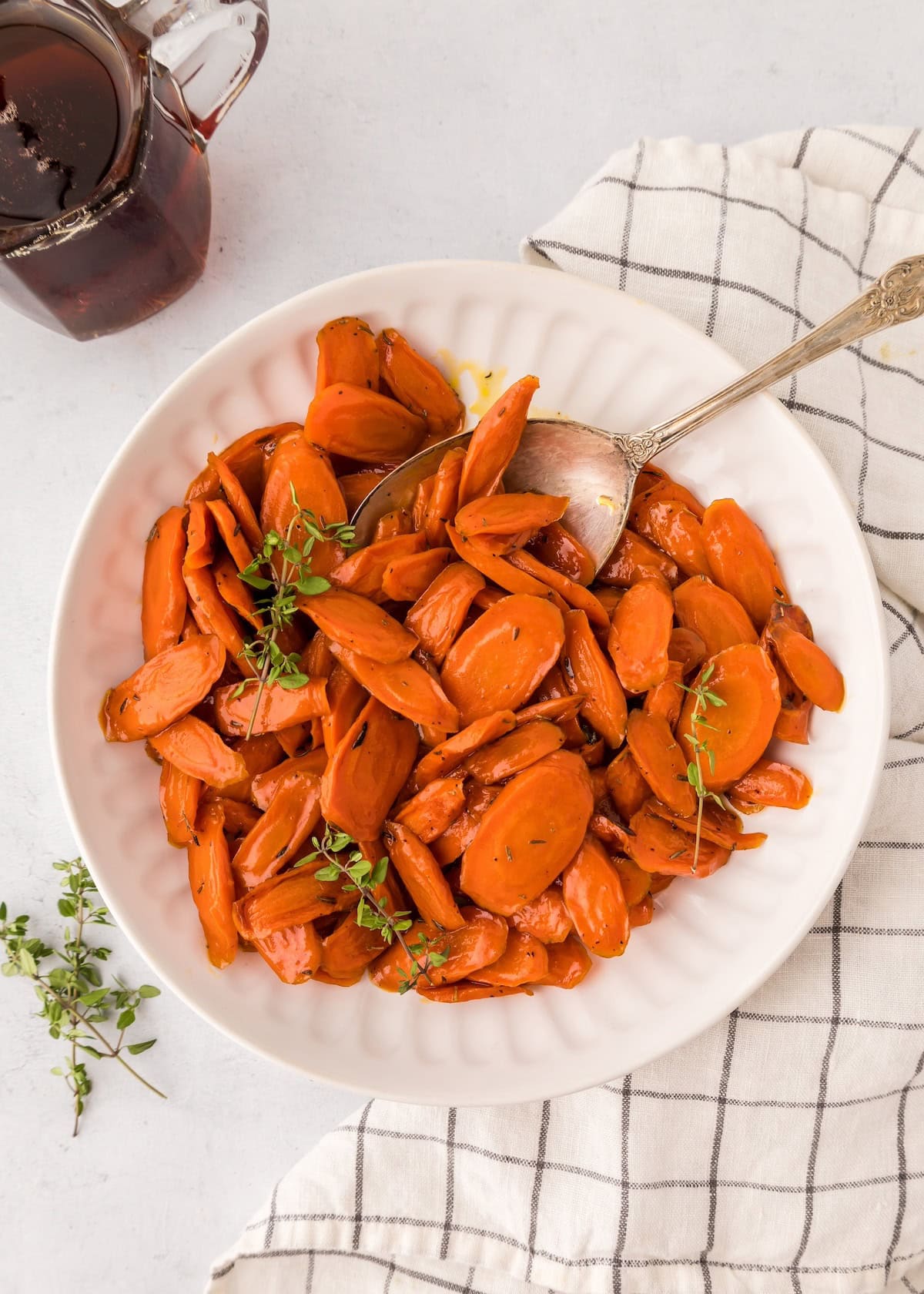 Sliced roasted carrots on a white plate with herbs and a spoon, on a checkered cloth.