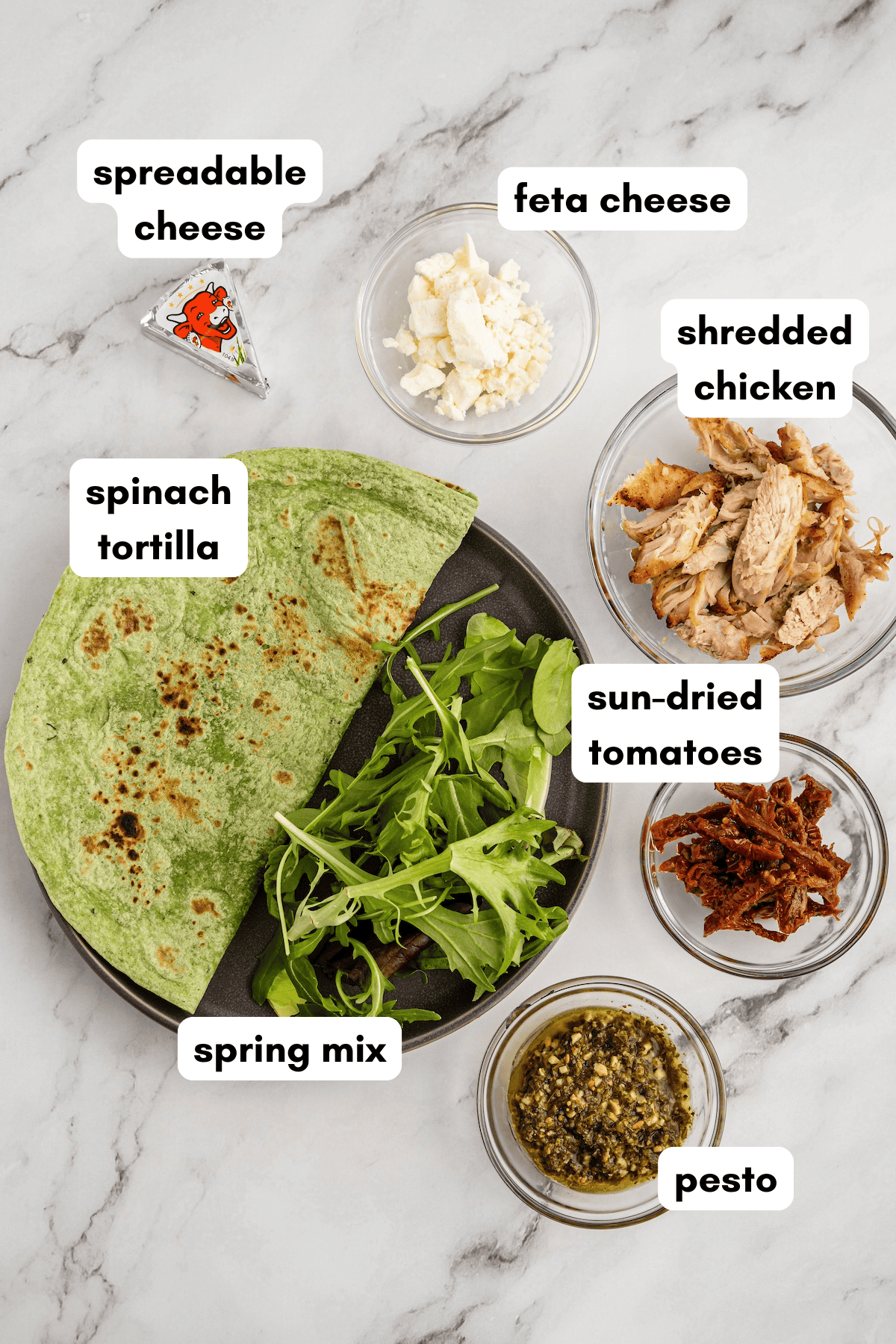 A plate with spinach tortilla, spring mix, pesto, cheese, shredded chicken, and sun-dried tomatoes.