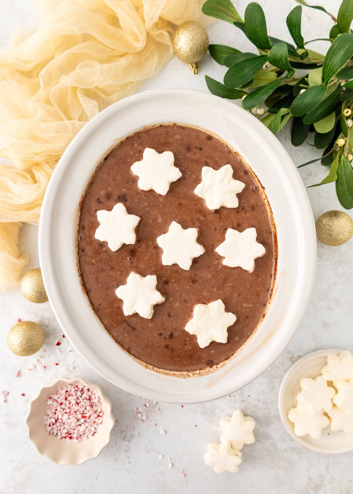 Oval dish of hot chocolate topped with star-shaped marshmallows, with festive decor nearby.