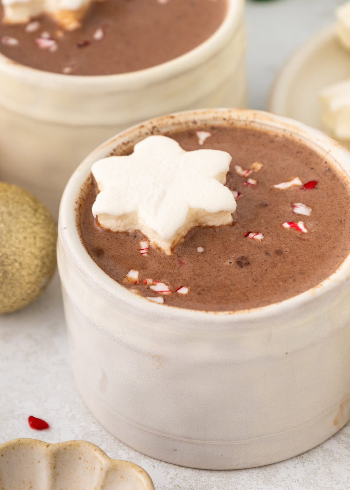 A mug of hot chocolate topped with a snowflake-shaped marshmallow and peppermint pieces.