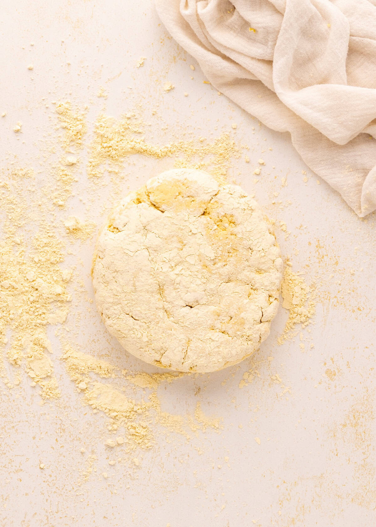 A round dough disc for Greek Yogurt Bagels, dusted with flour on a light surface, cloth nearby.