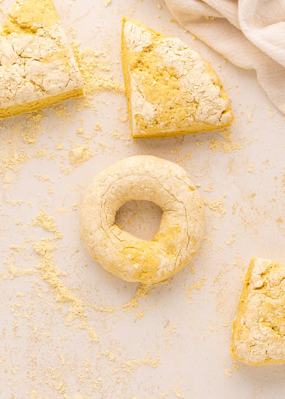 Round and triangular Greek Yogurt Bagels dough on a lightly floured surface, cloth in the corner.