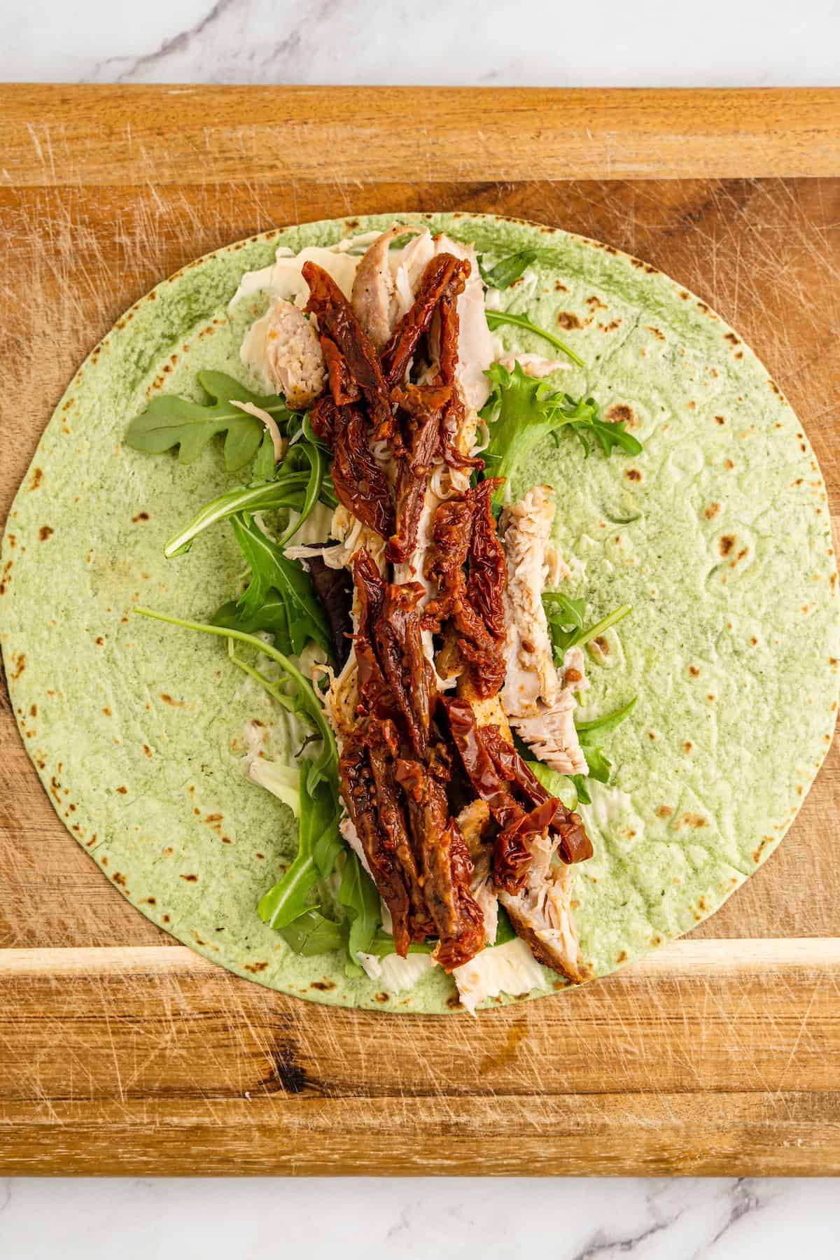 A spinach wrap with chicken, arugula, and sun-dried tomatoes on a wooden board.